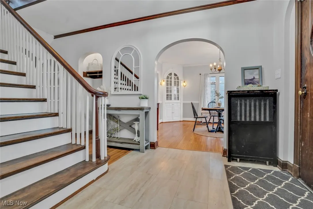 Entrance foyer with arched walkways, stairway, crown molding, wood finished floors, and a chandelier