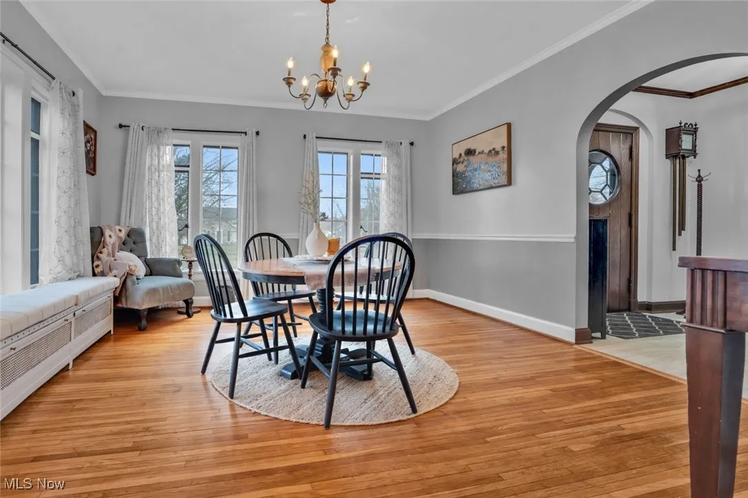 Dining area with light wood-style floors, ornamental molding, a chandelier, arched walkways, and baseboards