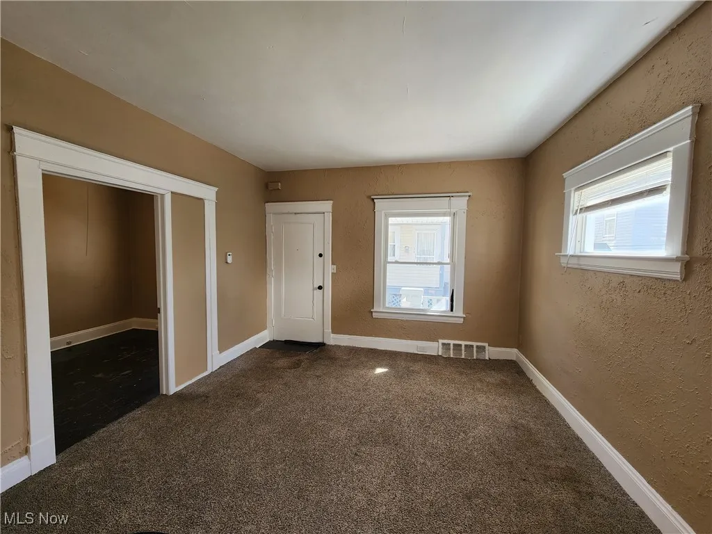 Empty room featuring dark colored carpet, baseboards, and a textured wall