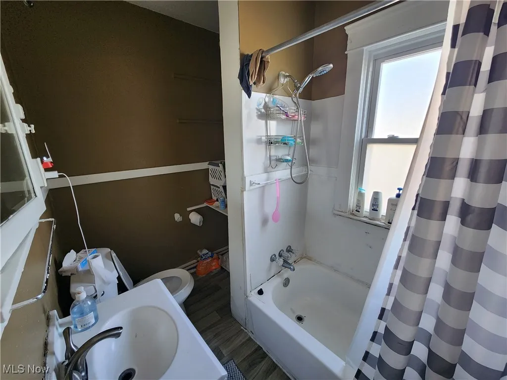 Full bath with a sink, shower / bath combo, and wood finished floors