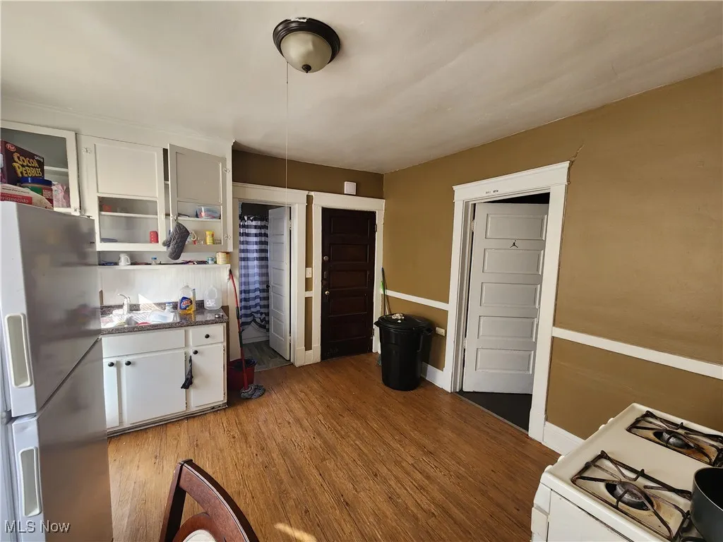 Kitchen with stainless steel refrigerator with ice dispenser, white gas range, light wood finished floors, a sink, and white cabinets