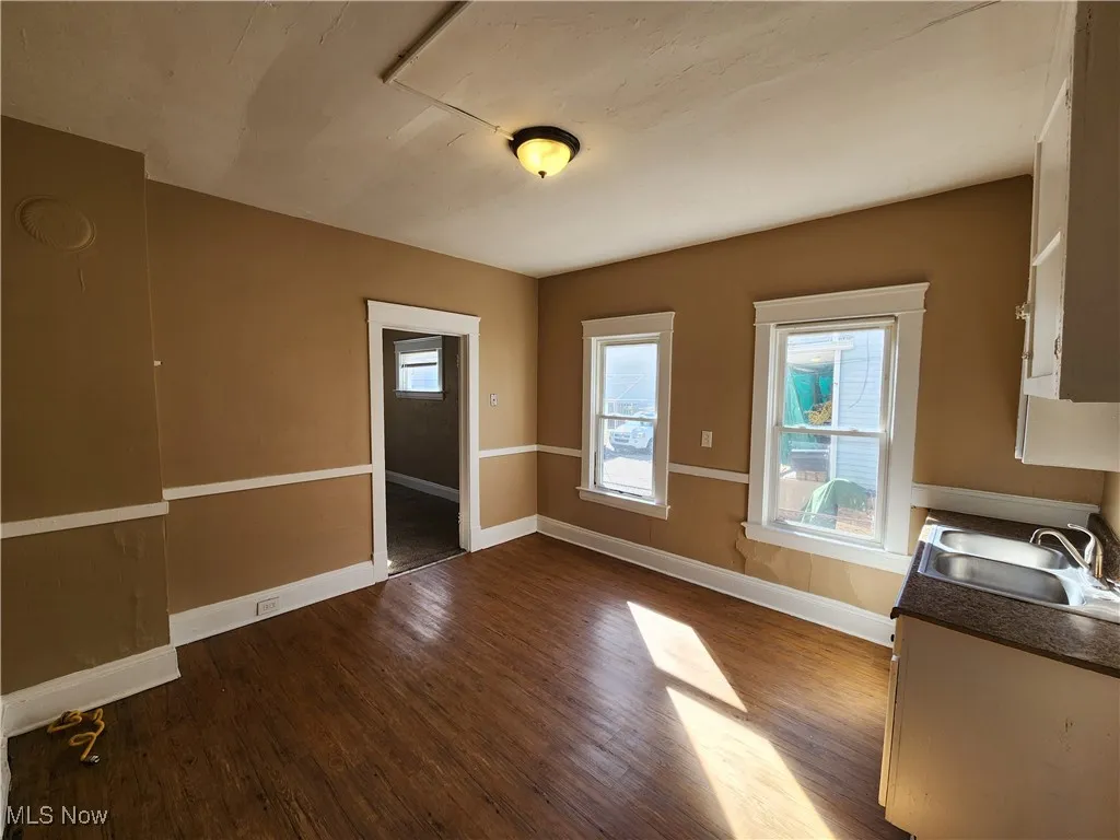 Unfurnished dining area with a sink, dark wood-type flooring, and baseboards