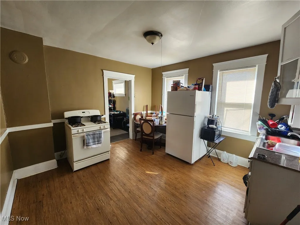 Kitchen with white appliances, dark wood-style floors, baseboards, dark countertops, and a sink