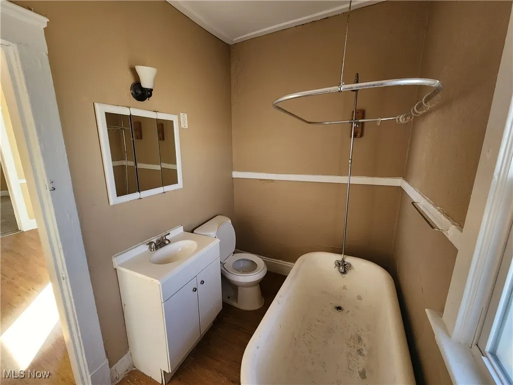 Full bath with wood finished floors, a tub to relax in, toilet, vanity, and baseboards