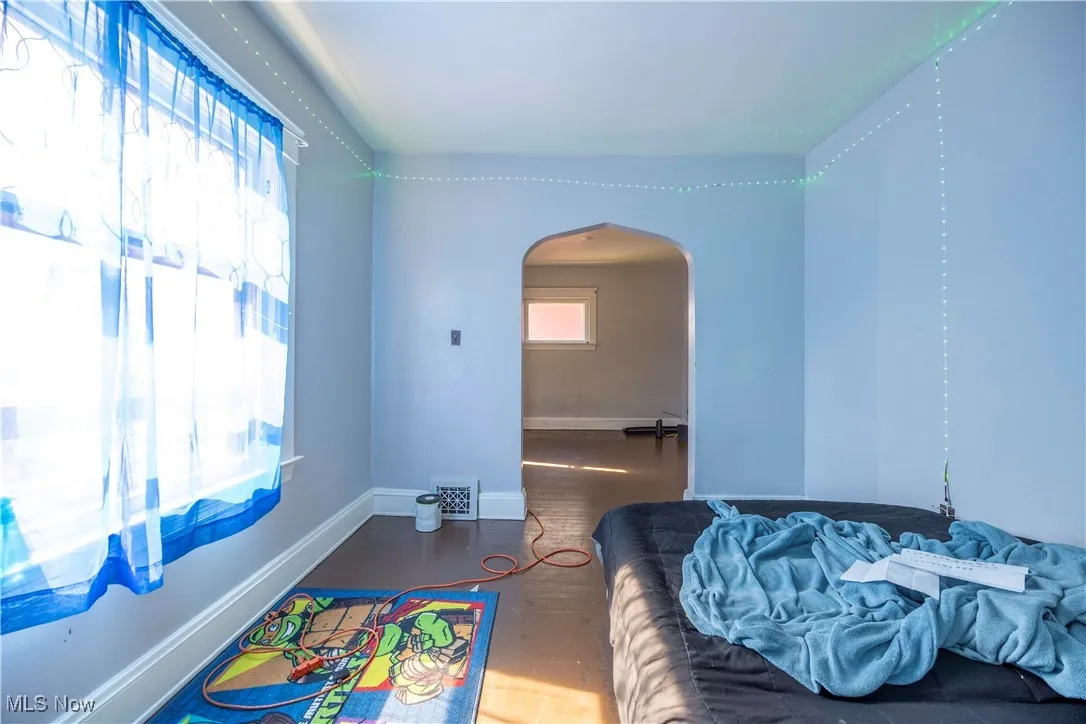 Bedroom with arched walkways, wood finished floors, and baseboards