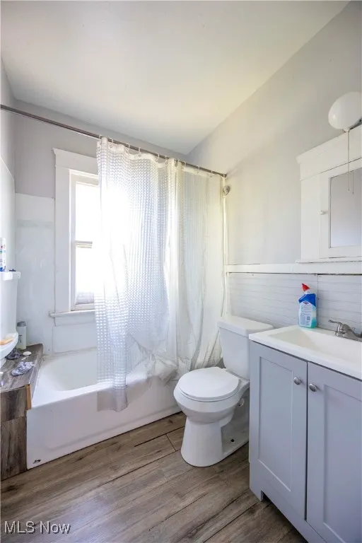 Full bath featuring toilet, a wainscoted wall, shower / tub combo with curtain, vanity, and wood finished floors