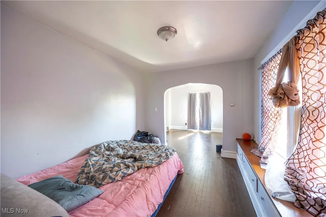 Bedroom featuring arched walkways, dark wood-style flooring, and baseboards