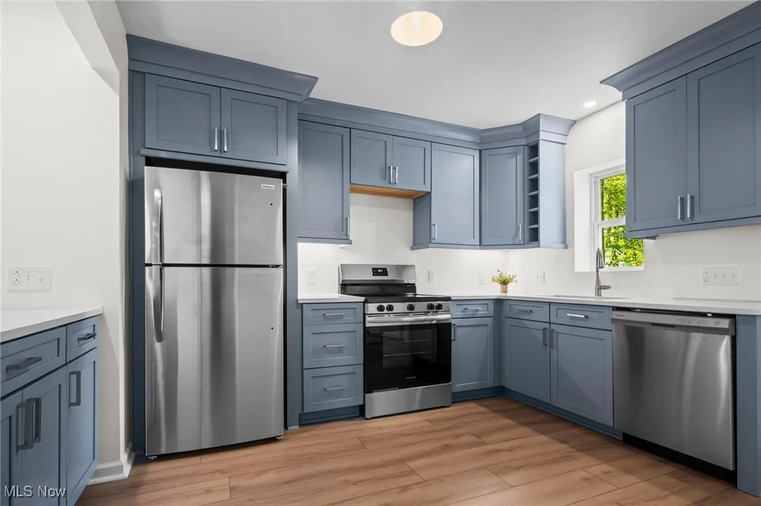 Kitchen with appliances with stainless steel finishes, a sink, light countertops, light wood finished floors, and recessed lighting