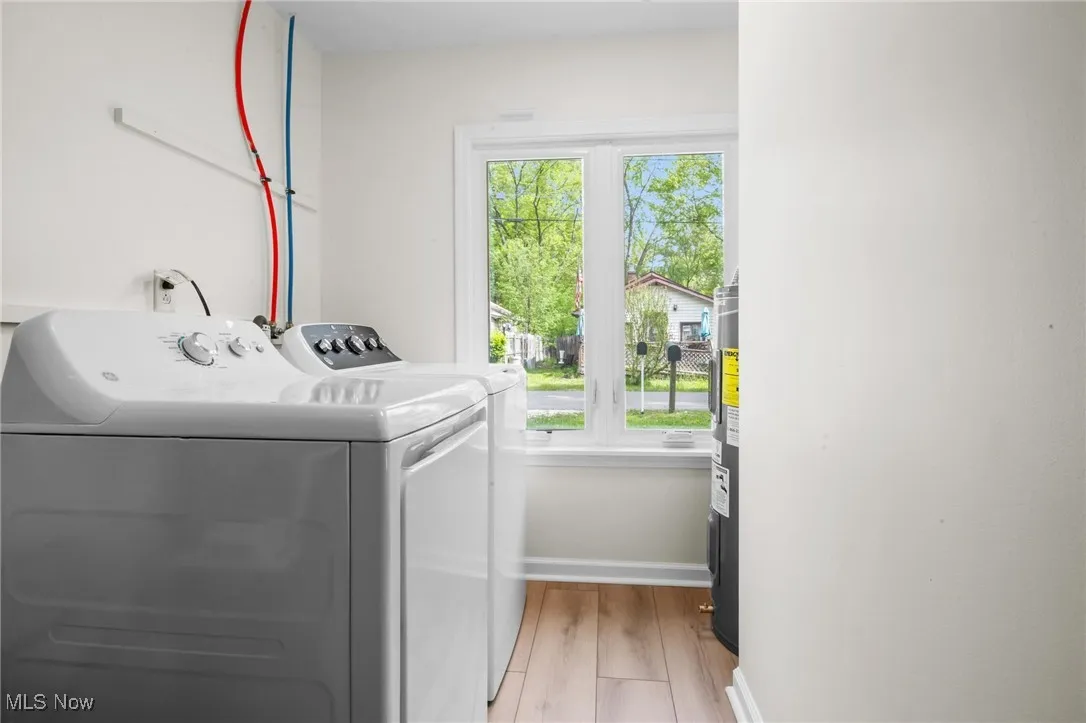 Laundry room featuring washer and clothes dryer, light wood-style flooring, baseboards, and electric water heater