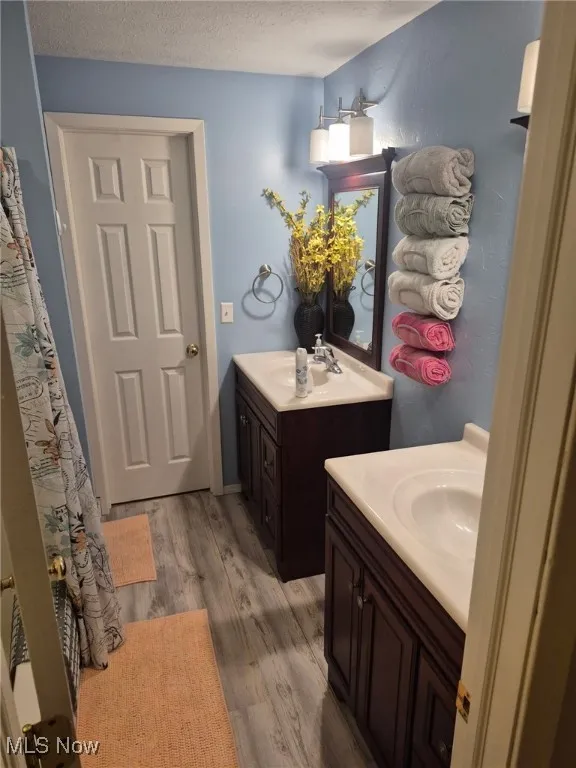 Bathroom with two vanities, wood finished floors, and a textured ceiling