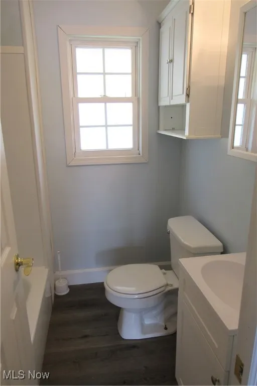 Bathroom featuring wood finished floors, toilet, vanity, a bathtub, and baseboards