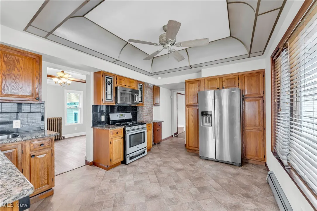Kitchen with appliances with stainless steel finishes, a baseboard heating unit, backsplash, and light stone countertops