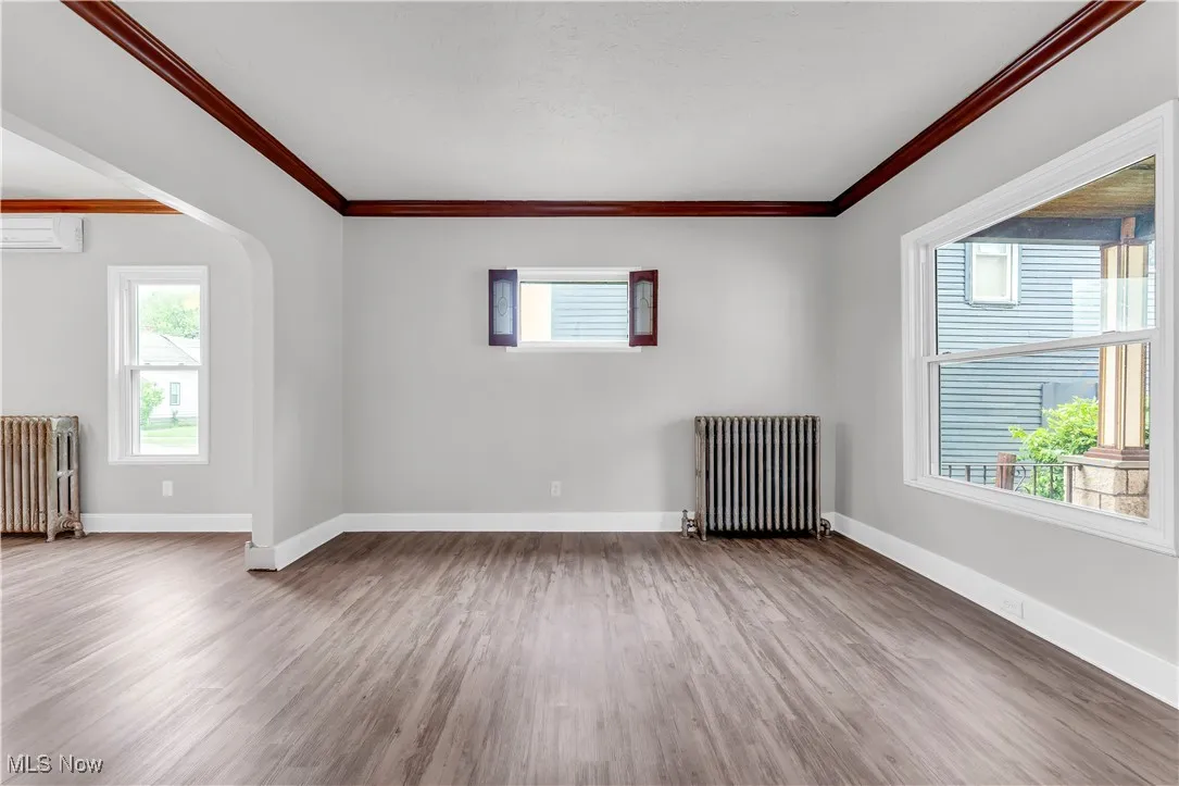 Unfurnished room featuring radiator heating unit, a wall mounted AC, wood finished floors, crown molding, and baseboards