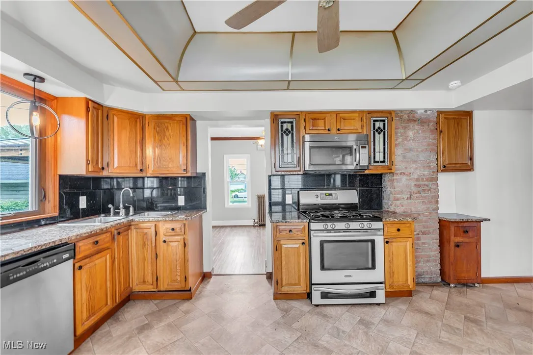Kitchen with appliances with stainless steel finishes, a ceiling fan, a sink, baseboards, and decorative backsplash