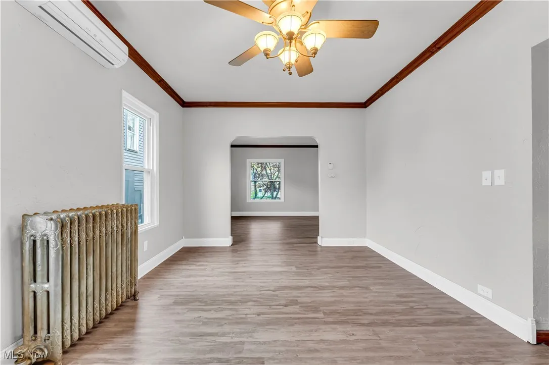 Empty room featuring radiator, an AC wall unit, arched walkways, ceiling fan, and wood finished floors