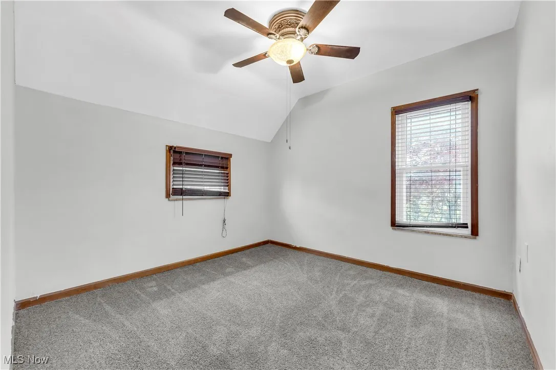 Carpeted empty room featuring baseboards, ceiling fan, and vaulted ceiling