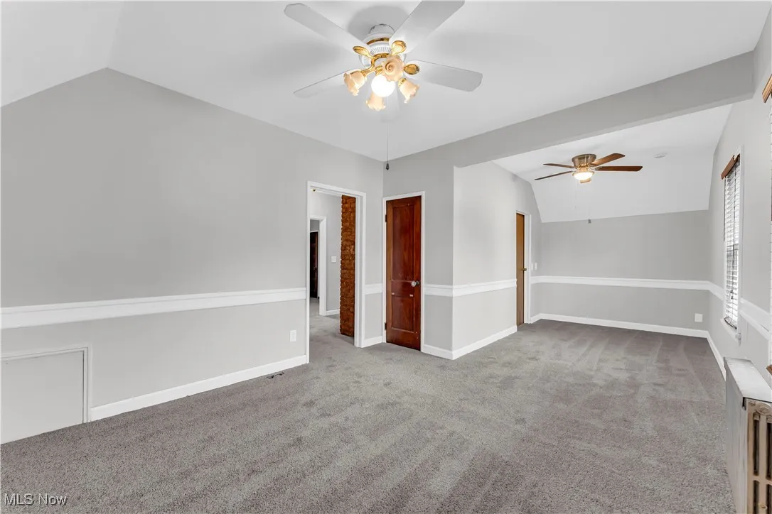 Unfurnished room featuring ceiling fan, vaulted ceiling, carpet flooring, and baseboards