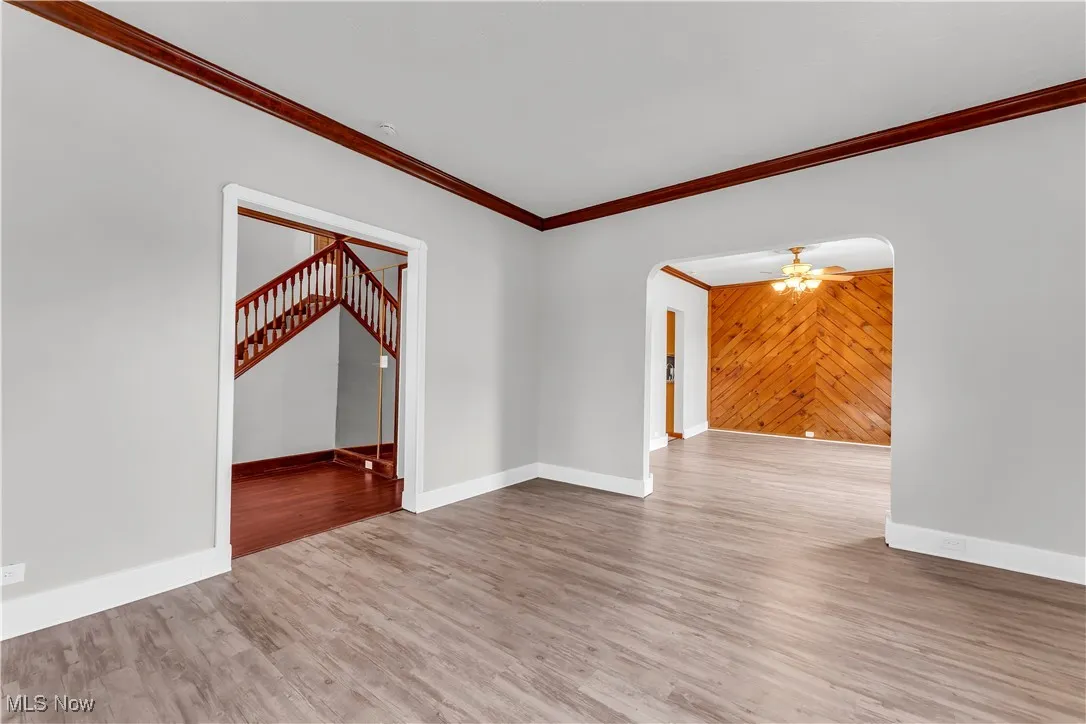 Spare room with arched walkways, ornamental molding, baseboards, wood finished floors, and stairs
