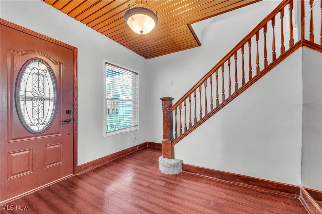 Foyer entrance featuring stairway, dark wood-style floors, baseboards, and wooden ceiling
