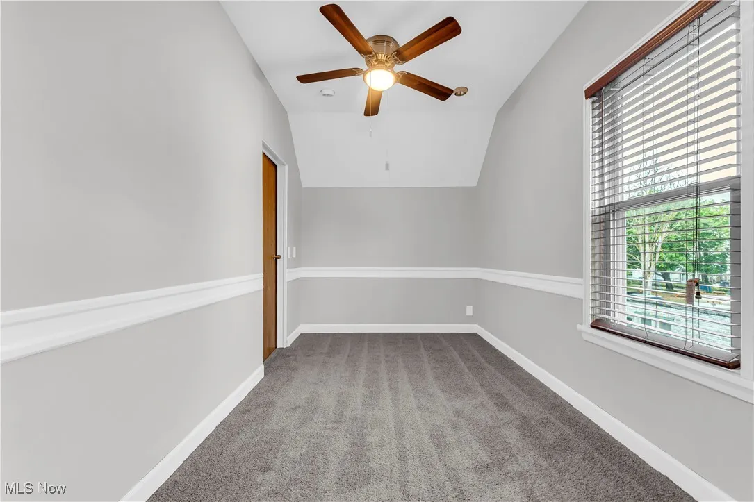 Carpeted empty room featuring lofted ceiling, ceiling fan, and baseboards