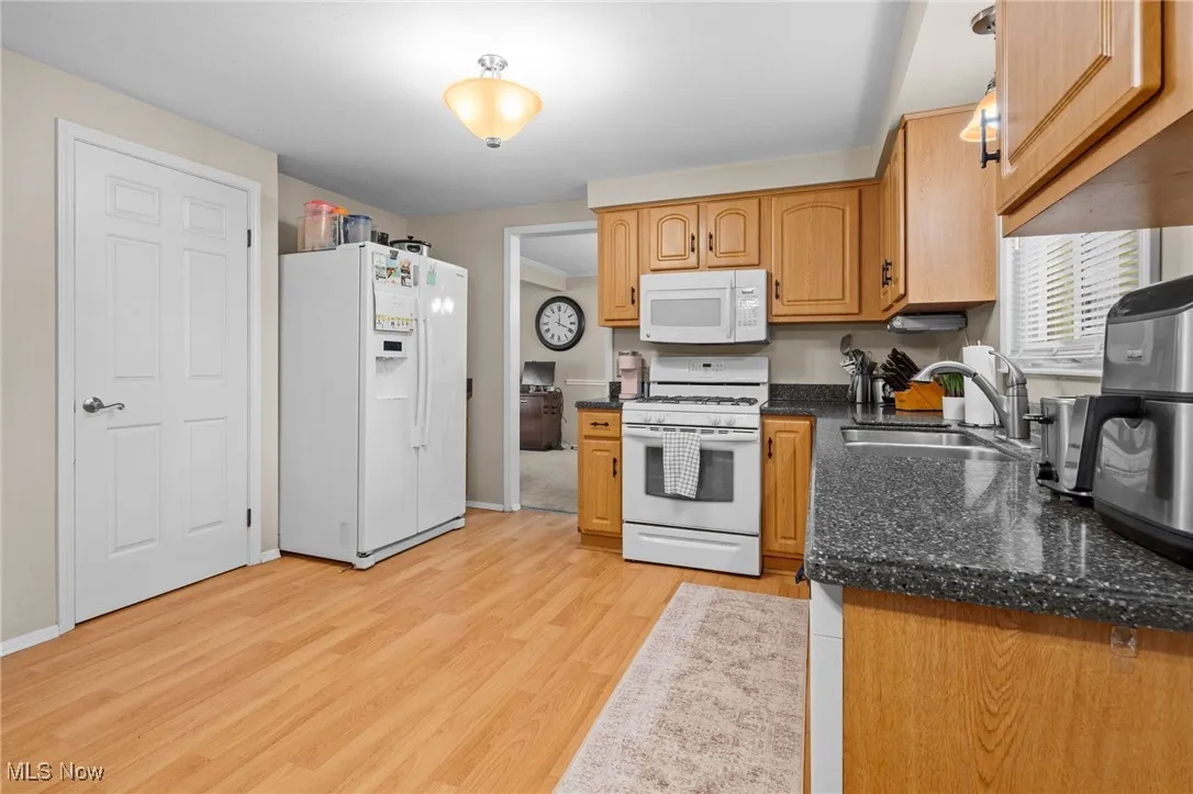 Kitchen with white appliances, light wood-type flooring, and dark stone countertops