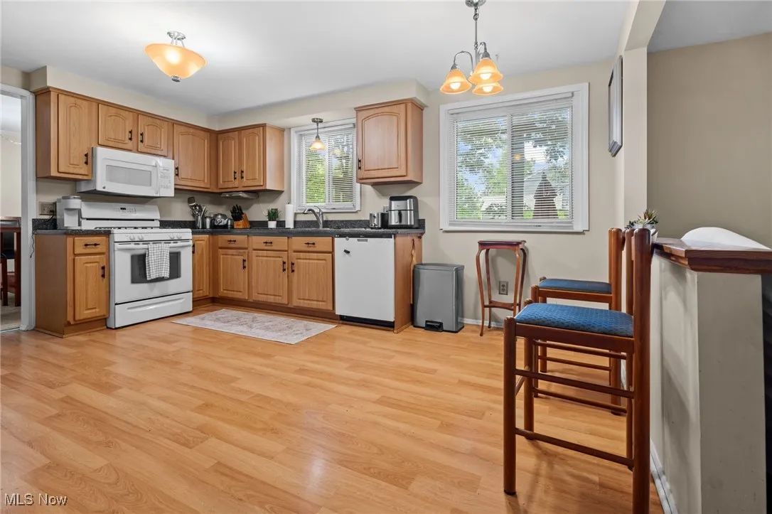 Kitchen featuring white appliances, light wood-style floors, dark countertops, hanging light fixtures, and a chandelier