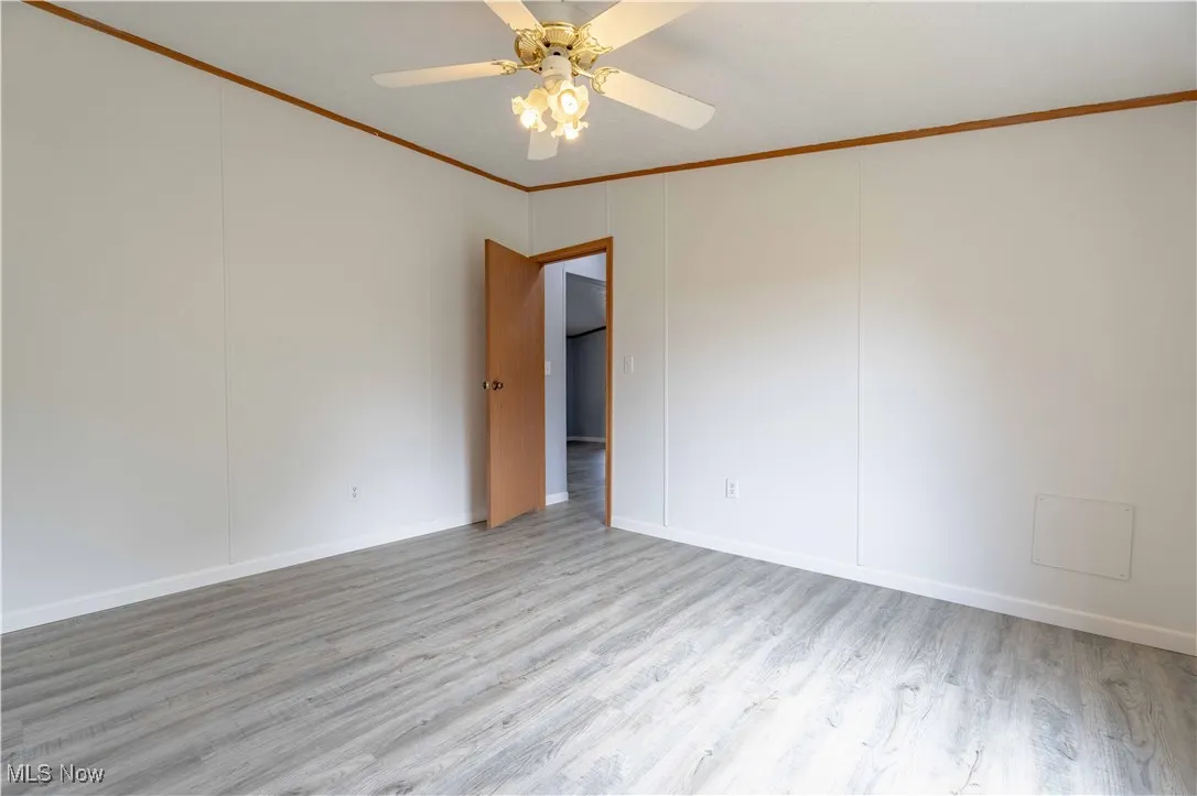 Empty room featuring ornamental molding, wood finished floors, and a ceiling fan
