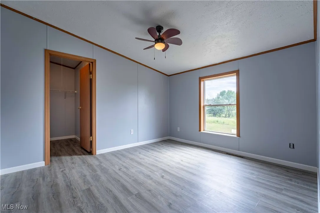 Unfurnished bedroom featuring a walk in closet, ornamental molding, light wood-style floors, ceiling fan, and a textured ceiling