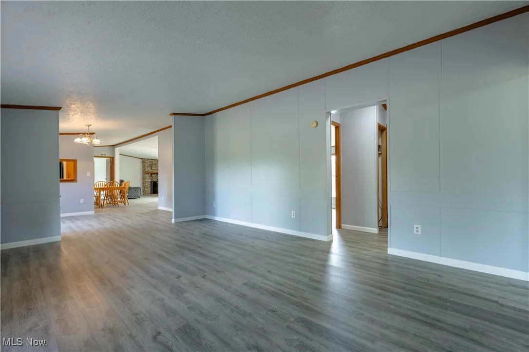 Unfurnished living room featuring crown molding, wood finished floors, a textured ceiling, and a chandelier