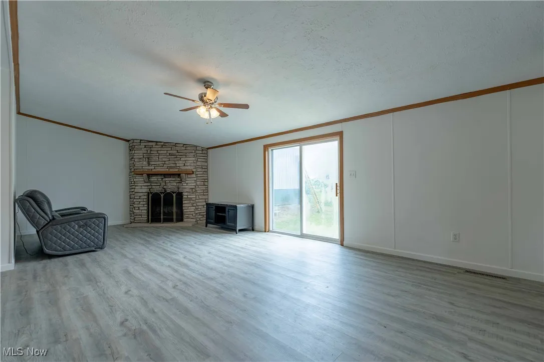 Unfurnished living room featuring a large fireplace, a textured ceiling, light wood-style flooring, a ceiling fan, and crown molding