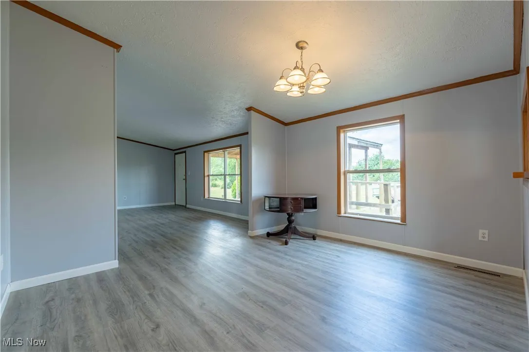 Unfurnished living room featuring healthy amount of natural light, light wood-style floors, a chandelier, a textured ceiling, and crown molding