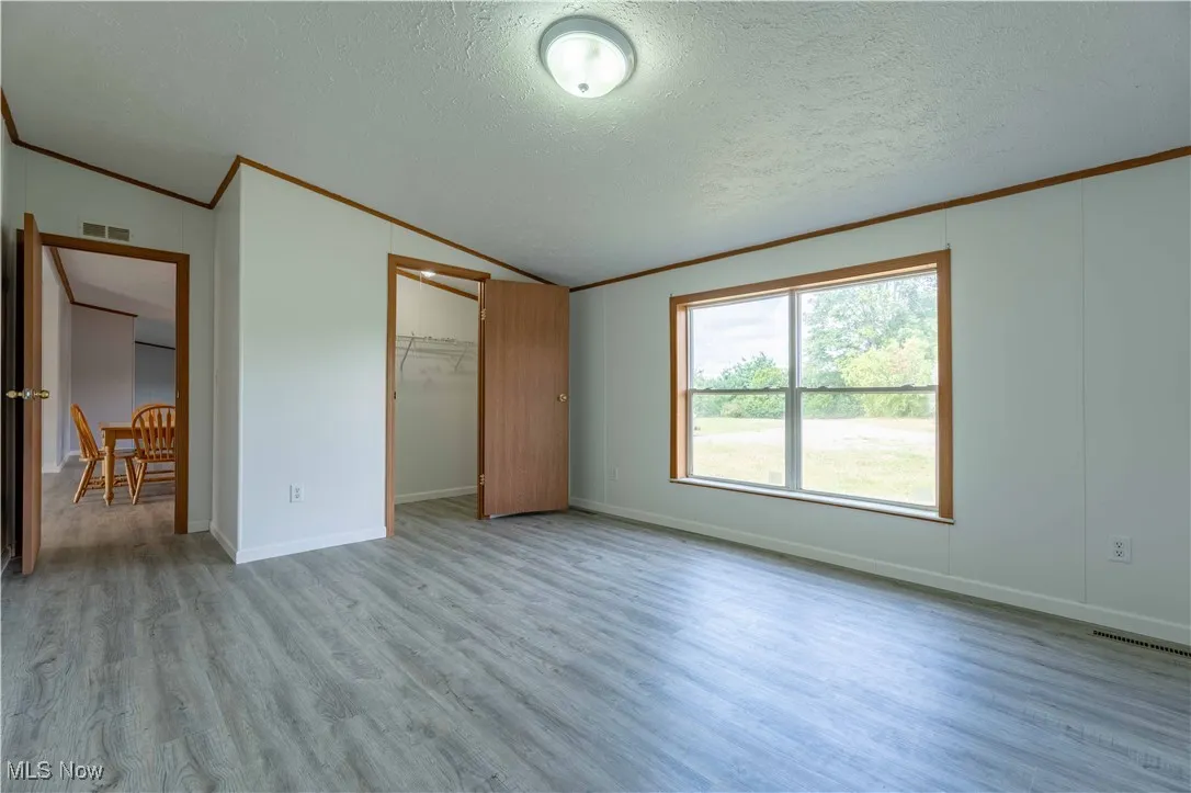 Unfurnished bedroom with crown molding, lofted ceiling, light wood-style floors, and a textured ceiling