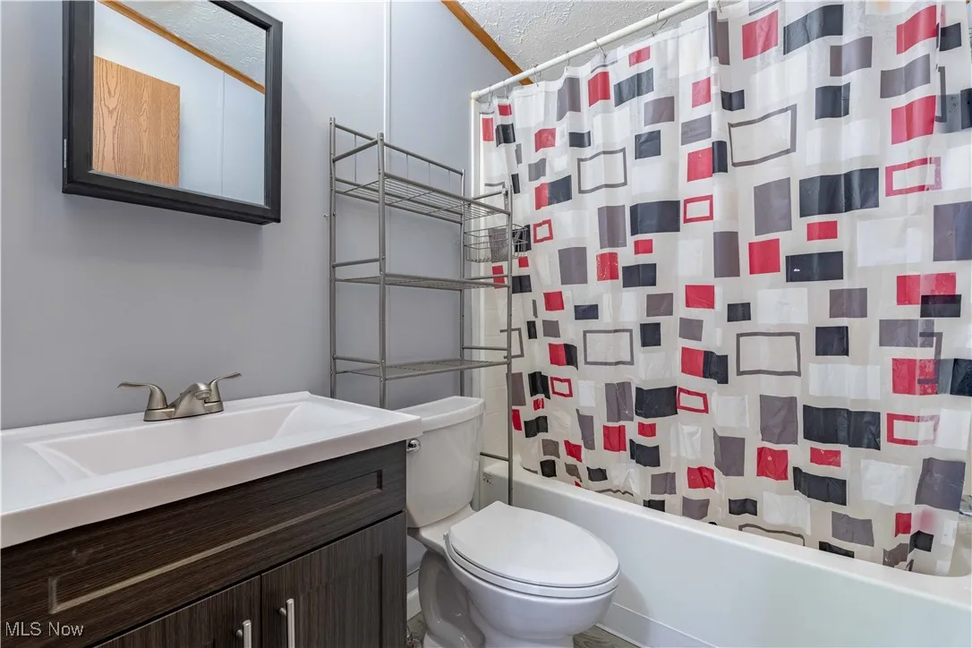 Bathroom featuring shower / bath combination with curtain, vanity, and a textured ceiling