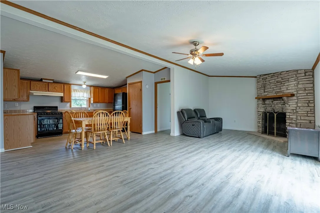 Living room featuring light wood-style floors, a textured ceiling, a stone fireplace, ceiling fan, and lofted ceiling