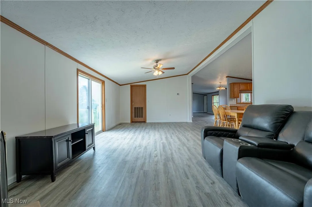 Living room featuring light wood finished floors, ornamental molding, lofted ceiling, a textured ceiling, and a ceiling fan