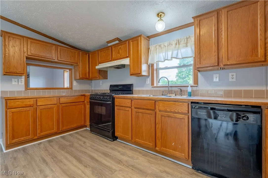 Kitchen featuring a textured ceiling, black appliances, vaulted ceiling, light wood-type flooring, and brown cabinetry
