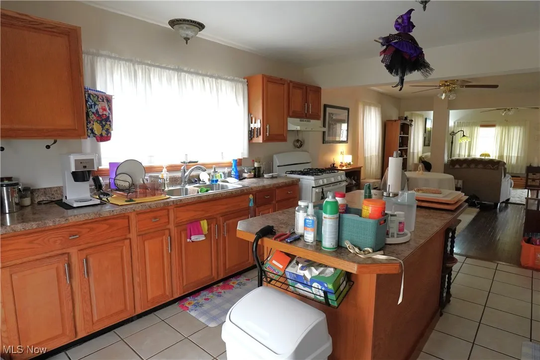 Kitchen featuring white gas range oven, under cabinet range hood, a sink, and light tile patterned floors
