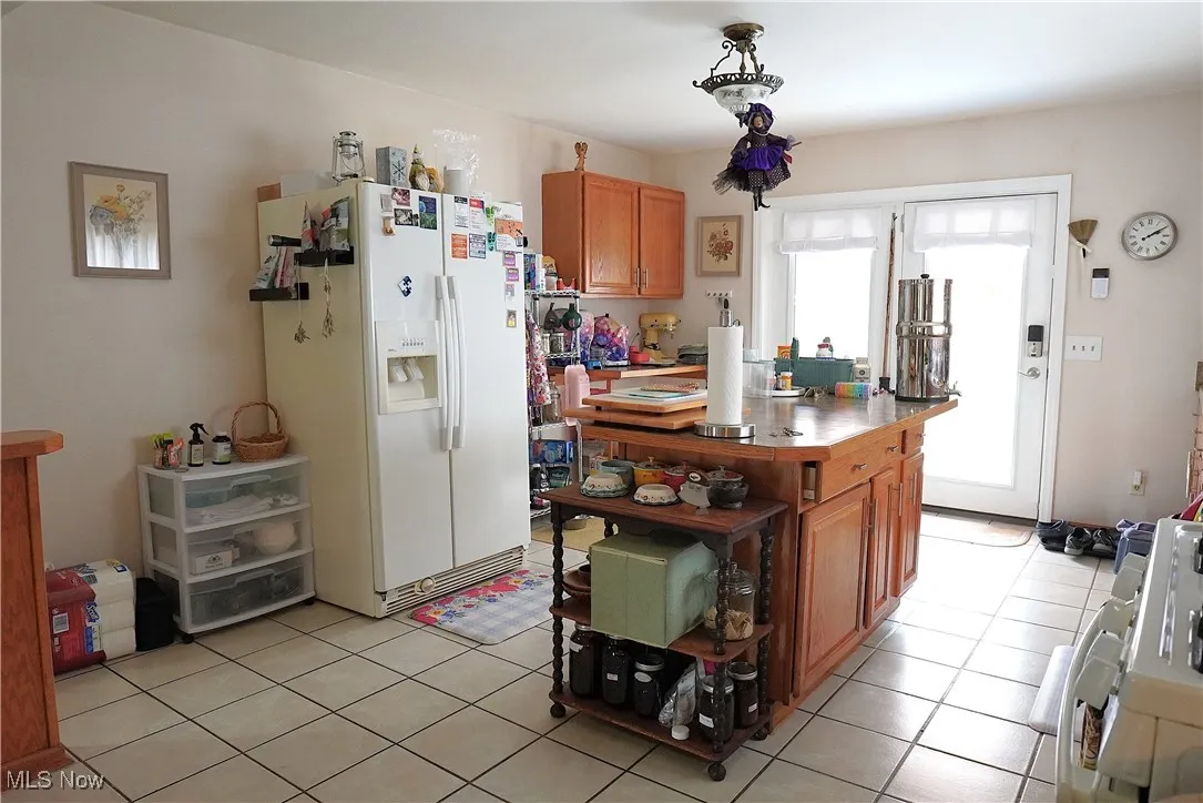 Kitchen featuring white refrigerator with ice dispenser, range, light tile patterned floors, and brown cabinets