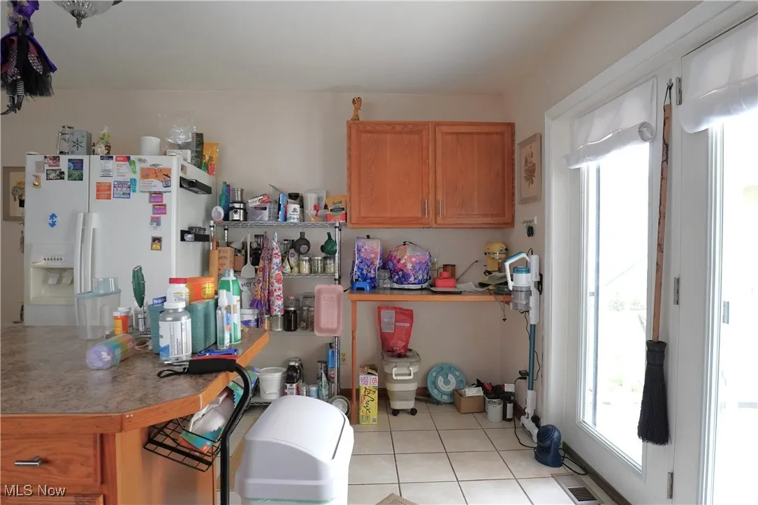 Kitchen featuring white refrigerator with ice dispenser, light tile patterned floors, and light countertops