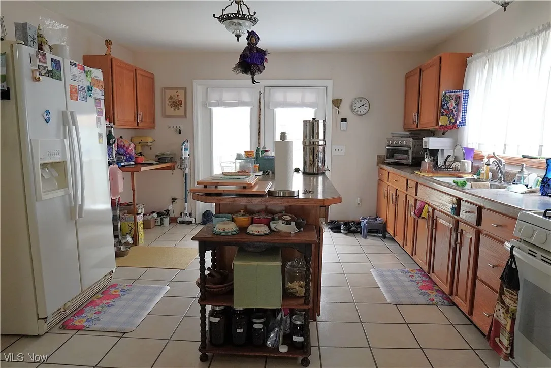 Kitchen featuring white appliances, a sink, brown cabinetry, open shelves, and light tile patterned floors