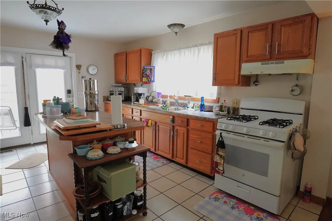 Kitchen featuring white gas range, under cabinet range hood, a sink, brown cabinets, and light tile patterned floors