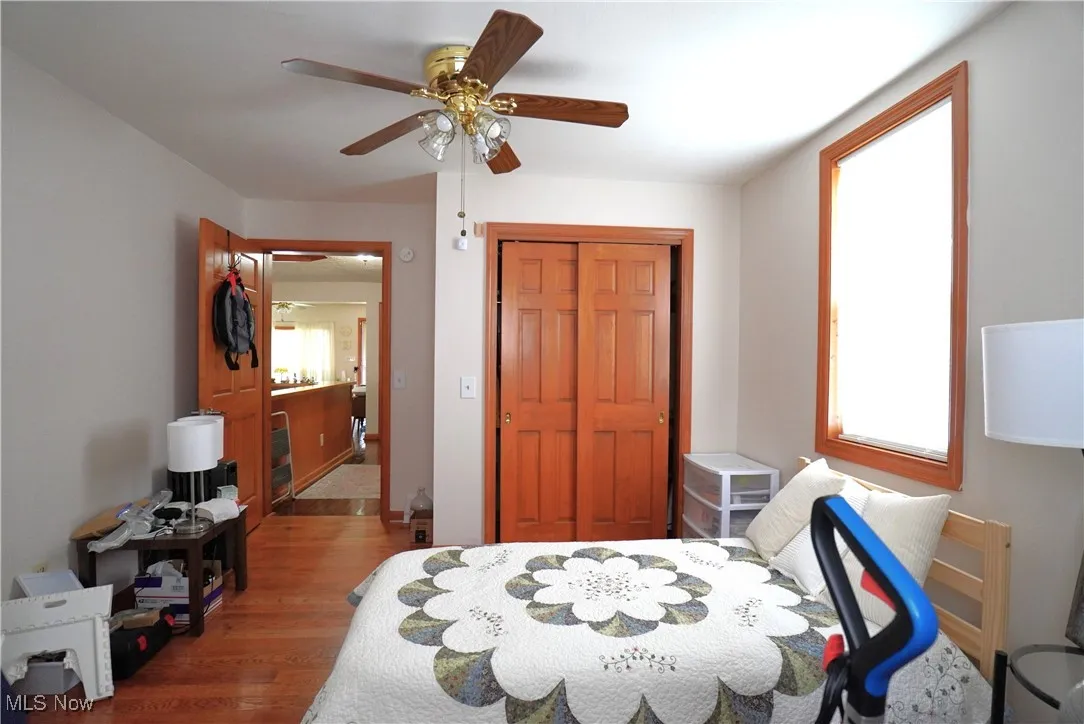 Bedroom with wood finished floors, multiple windows, ceiling fan, and a closet