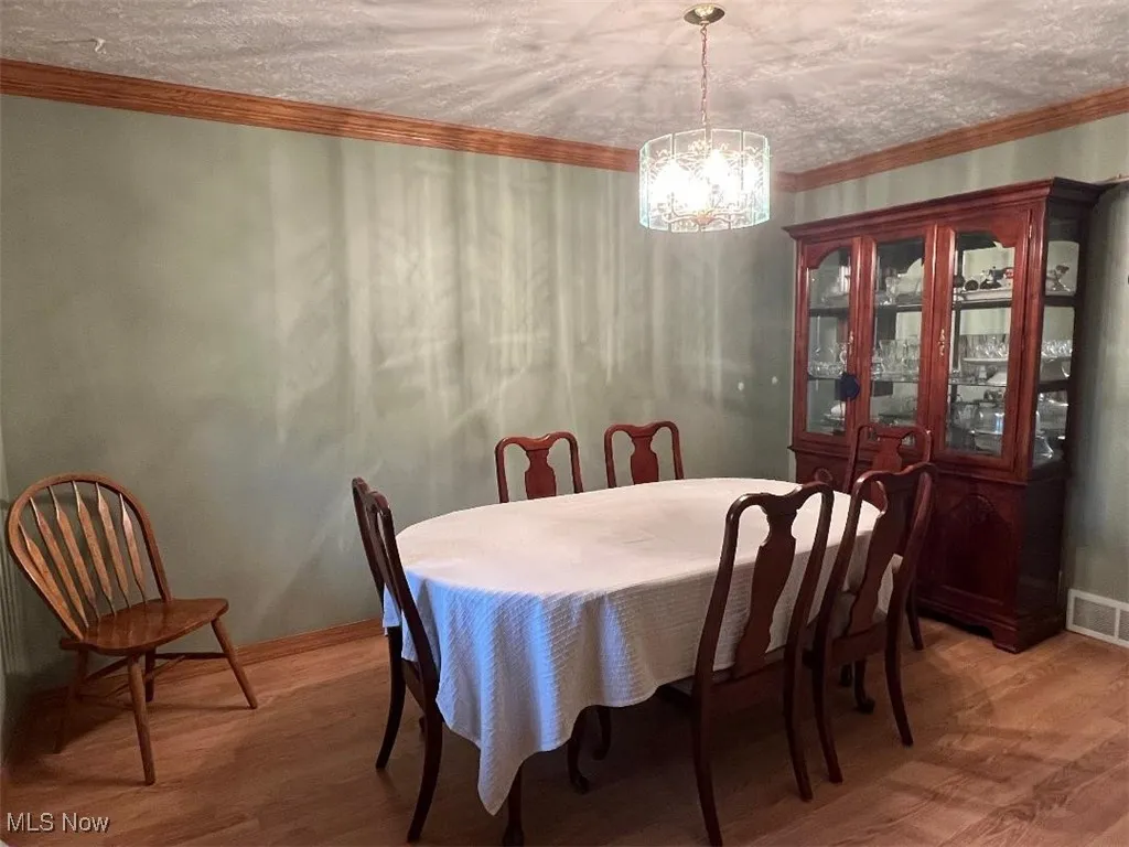 Dining area with a chandelier, light wood-style flooring, baseboards, and ornamental molding