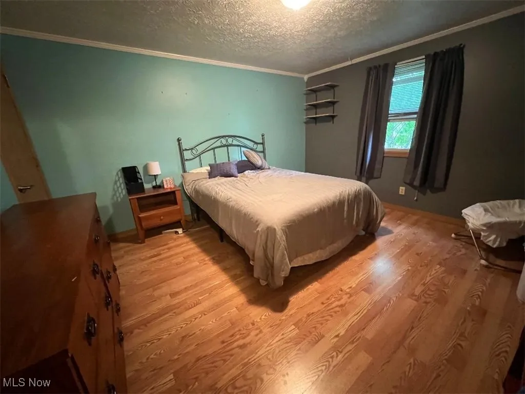Bedroom with ornamental molding, laminate floors, a textured ceiling, and baseboards