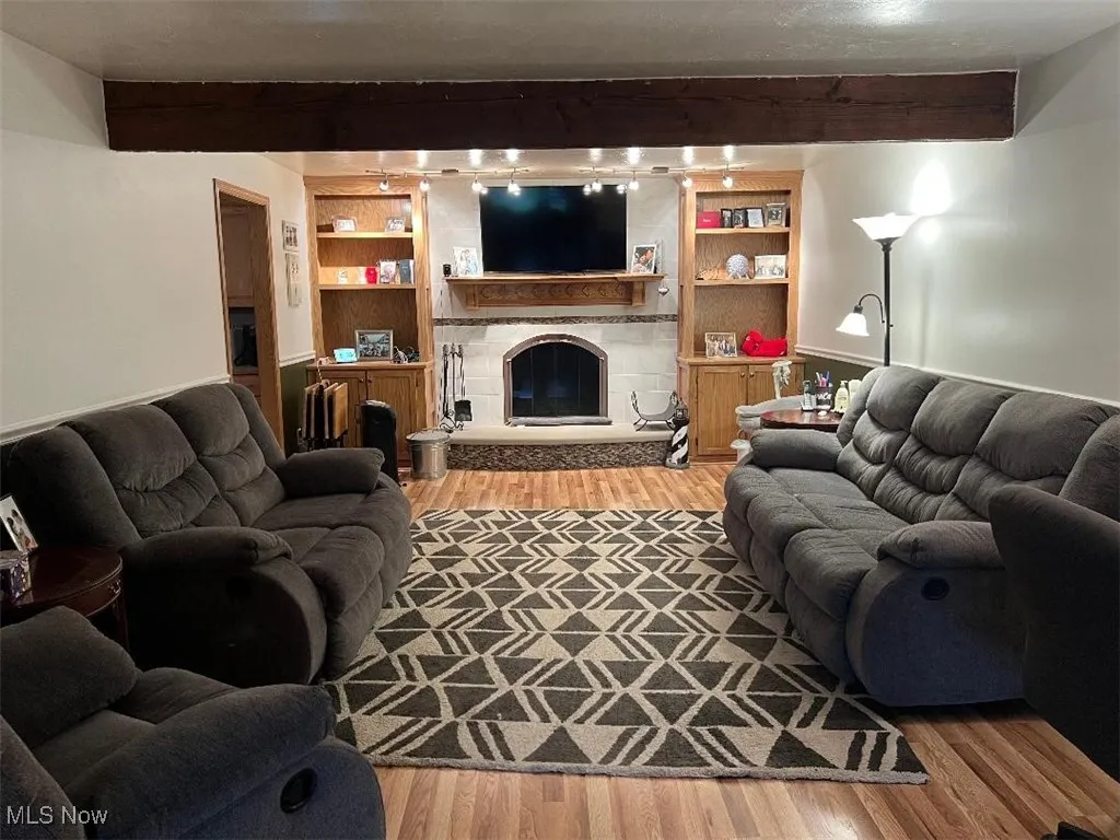 Living area featuring beam ceiling, wood finished floors, a fireplace, and built in shelving & cabinetry