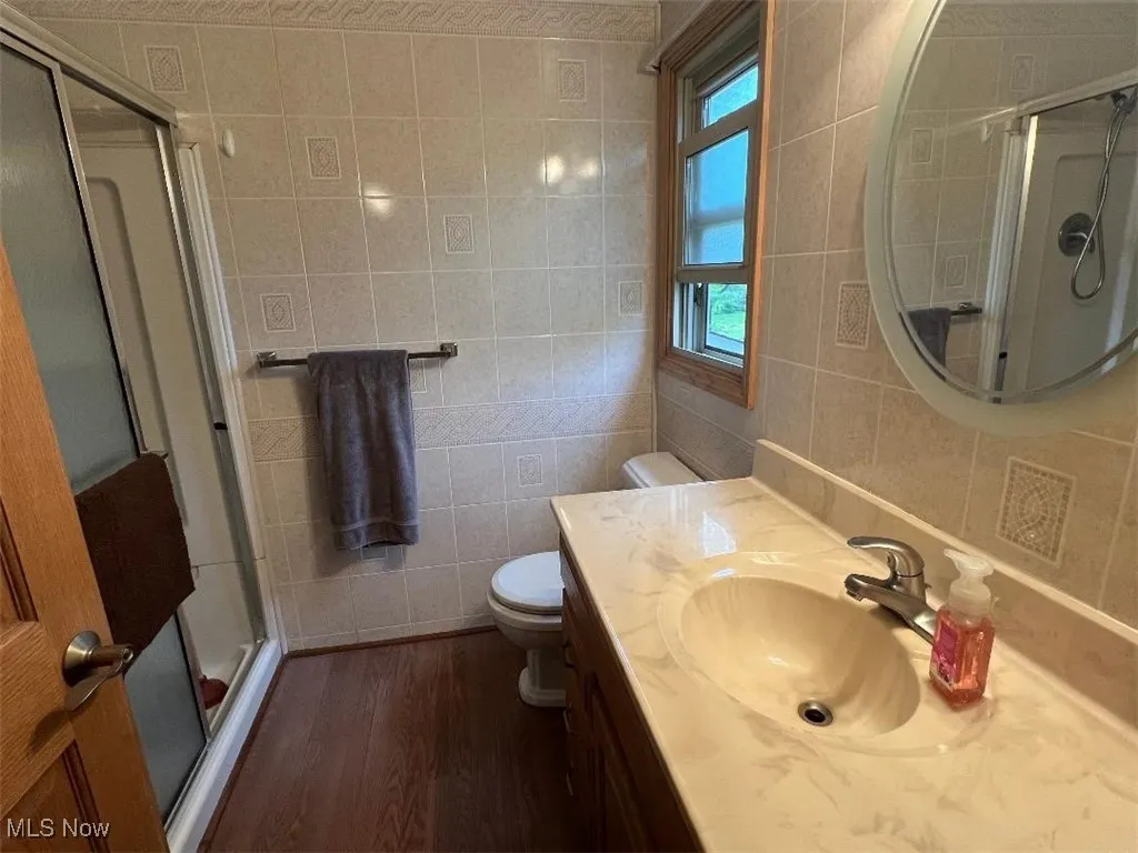 En suite with tile walls, laminate floors, a shower stall, toilet, and vanity