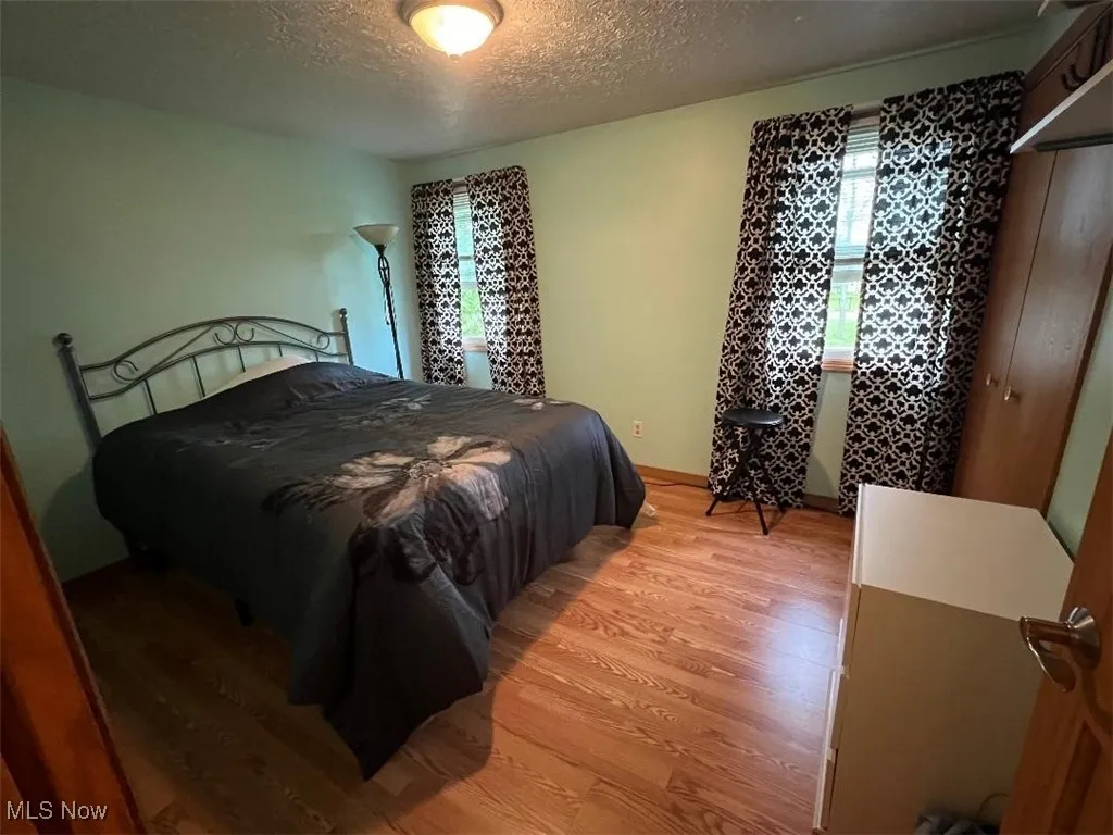 Bedroom with light wood-type flooring, a textured ceiling, and baseboards