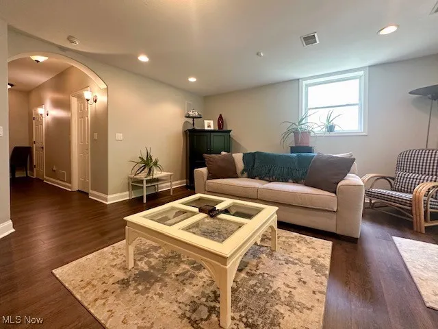 Living room featuring arched walkways, dark wood-style flooring, baseboards, and recessed lighting