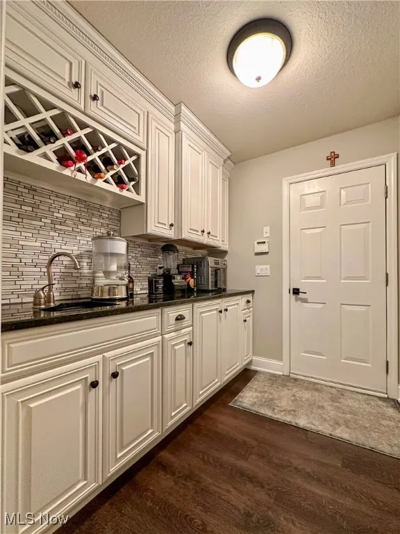 Butlers Pantry featuring dark wood-type flooring, backsplash, baseboards, a sink, and a textured ceiling