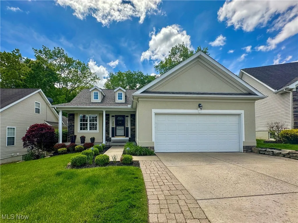 View of front facade featuring stucco siding, stone siding, a front lawn, driveway, and an attached garage